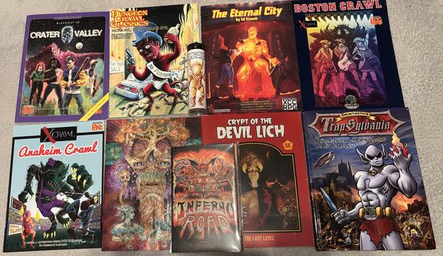 The covers for Blackout in Crater Valley, Xcrawl: New Year’s Evil, The Eternal City, Boston Crawl, Anaheim Crawl, Hobonomicon #4, Inferno Road, the Crypt of the Devil Lich stretch goal packet, Grimtooth’s Trapsylvania, and the Xcrawl Classics dice set.