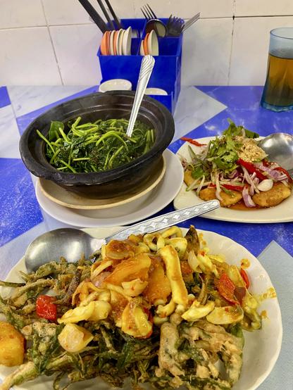 A plate of squid on top of a bed of deep-fried water convolvulus, a plate of spicy & sour tofu, and a clay pot filled with vegetables