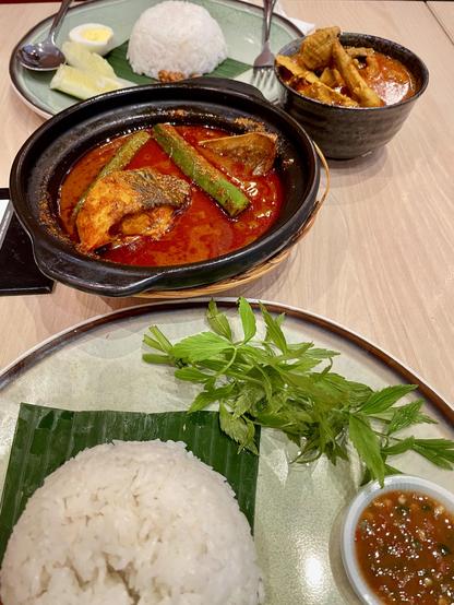 A plate of rice, some ulam, and a clay pot filled with stingray asam pedas