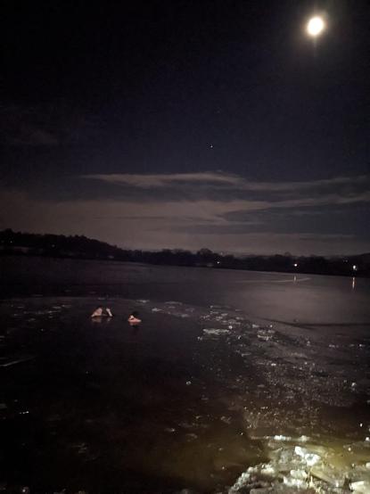 Me and a swim buddy skinny dipping in an icy reservoir in the winter evening near Buxton, UK. We are submerged up to our shoulders. The Moon and Mars are in the background in a beautiful, mostly clear sky.