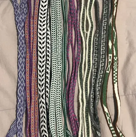 9 woven bands with colorful patterns arranged side by side on a grey blanket