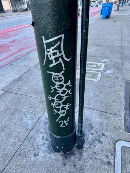 A tag on a streetpost with some kanji on top (that I don't know how to read) and a drawing of a caterpillar, with "25" written at the bottom. The drawing is done with silver metallic paint. The caterpillar is made up of 8 circles in a row and tiny stick figure-like legs and antenna.