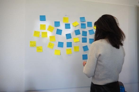 Photo montrant une participante regardant les propositions réalisées sur des post-it collés sur un tableau blanc.