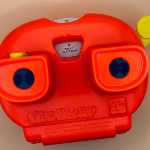 An orange View-Master toy with two circular viewing lenses and a label indicating "Vermont Horse Farm" is visible. The device is designed for viewing 3D images.