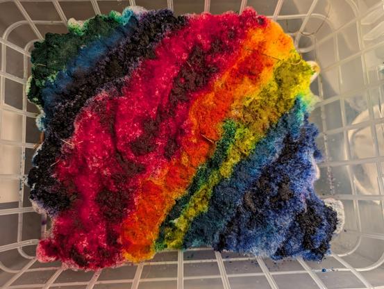 Top-down photo of rainbow colored snow piled up in a plastic bin over a big plastic grate. 

Color order: green, blue, purple, pink, magenta, orange-red, gold, green, blue, darker blue