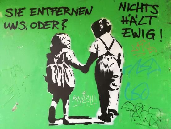 Ein Junge und ein Mädchen gehen innig Hand in Hand. Gesprüht in Schwarz-Weiß mit Schablonentechnik. Über dem Mädchen steht: "Sie entfernen uns oder?". Der Junge antwortet: "Nichts hält ewig." Der Hintergrund in Grün darauf viele tags gekritzelt.