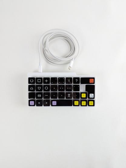 View from the top. The keyboard has black keys with basic LoCoS symbols printed on it. It can be plugged into a computer with a USB-C