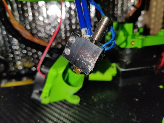 Close up of a 3D printer hot end, held in the air by two pairs of cables. Everything except the nozzle, heating unit and connection to the heatbrake is already disassembled.
