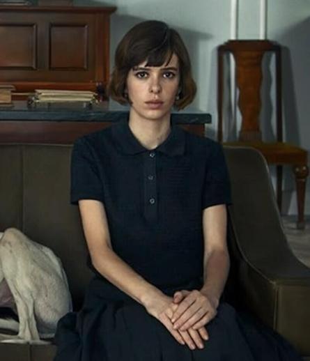 Alba Planas plays Hildegart Rodriguez as a teen in The Red Virgin. She sits on a bench with her hands folded looking seriously at the camera.