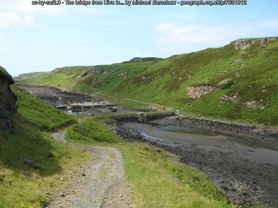 Green hills of two islands parted by a wide, shallow, ocean inlet.  The sea is crossed by a stone bridge