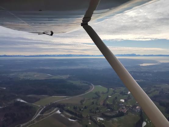Blick aus dem Flugzeug nach links unter Tragfläche. Die Alpenkette ist schön zu sehen und verschiedene Wolkenschichten.