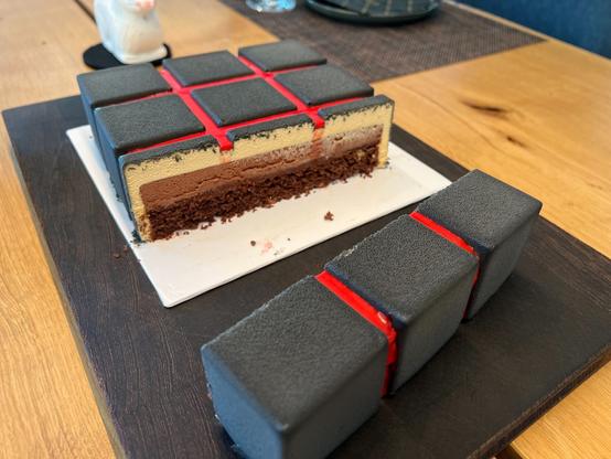 Cake sliced through, showing an outer layer of light chocolate mousse, a dark chocolate mousse, a chocolate cream, a cocoa biscuit and a crunchy bottom layer