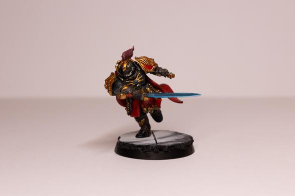 A Blade Champion model in black armour in a running pose. The armour has gold trim and red accents. He has a pink/red plume on his helmet and is swinging two large glowing blue swords. He is stood on a marble base.