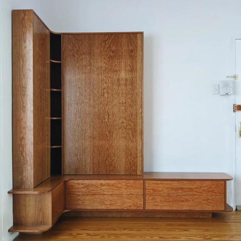 A custom cherry entryway bench and storage. The bench is an is a L shape and features 4 drawers and a small door. Above the bench are 2 large doors and a corner shelving unit.