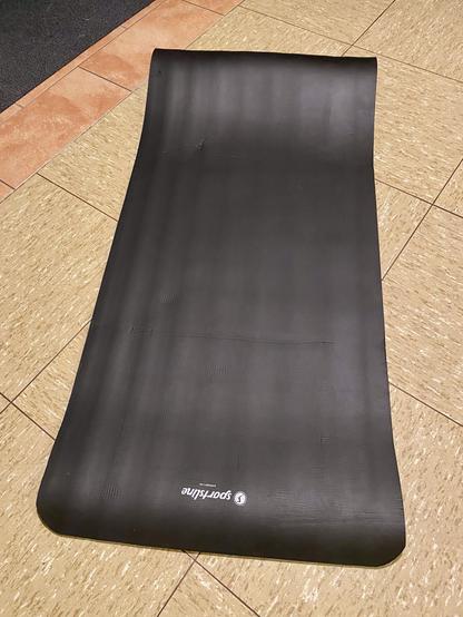 Eine schwarze Trainingsmatte ist auf einem Fliesenboden ausgelegt.