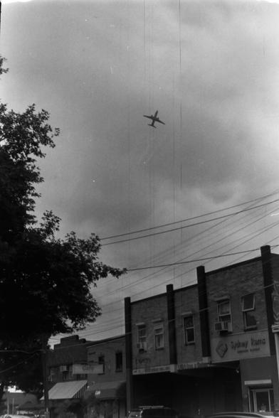 A plane taking off from Sydney airport, ascending and banking over a light industrial area. Shot in B&W. There are streaks down the middle, faintly, from the development of the film.