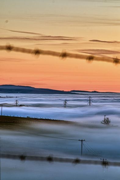 Barwed Wire and Pylons. Taken 26 December 2024 from Harbour Hill, Strinesdale, Oldham.  A view through blurred barbed wire shows pylons marching off into the low cloud south towards the Pennines.