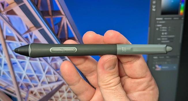 A hand holding a stylus pen with two shortcut buttons, against a background of a computer screen displaying architectural design.