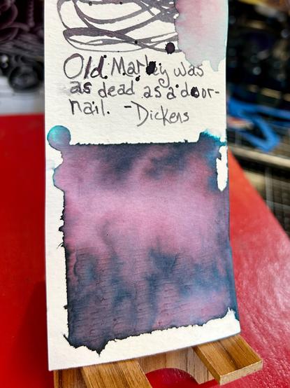 The bottom of the swatch has a square patch of ink. Water has been added and you can see vivid teal and rose tones in the purple gray ink. The very bottom of the square is distressed a little.

A quote is written in above the square. It reads:

“Old Marley was as dead as a door-nail.”, Dickens