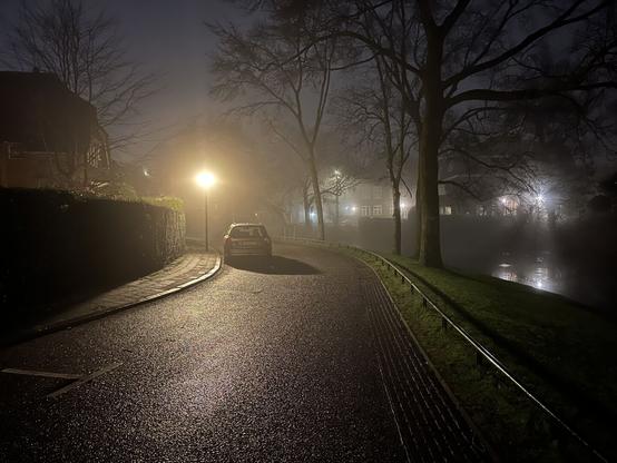 A streetlight draws a huge shadow of a single car on the damp street.