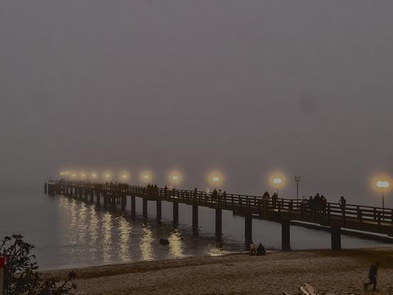 Beach with pier, illuminated by lamp posts on the pier.
