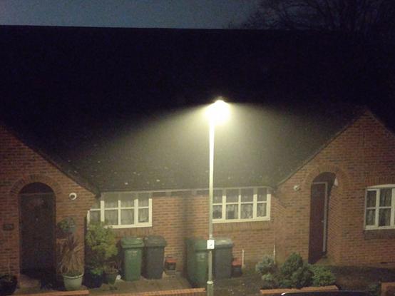 Photo of a house illuminated by a streetlamp. Due to the mist, the cone of light is well visible.