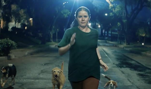 Amy Adams runs on a dark street. Several dogs are running behind her.