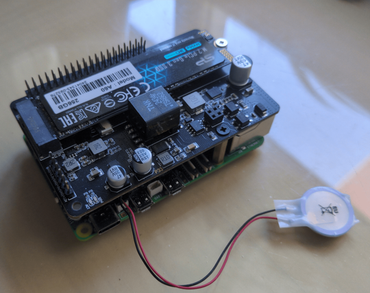 A Raspberry Pi 5 equipped with an NVMe SSD HAT for expanded high-speed storage. It features a neatly stacked design, with the HAT providing essential connectivity for the SSD while maintaining the compactness of the Pi. A small connected battery ensures real-time clock functionality.