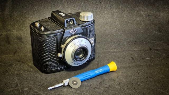 An Agfa Clack on a grey background. In the foreground is a laser cut pinhole propped against a small screwdriver.
