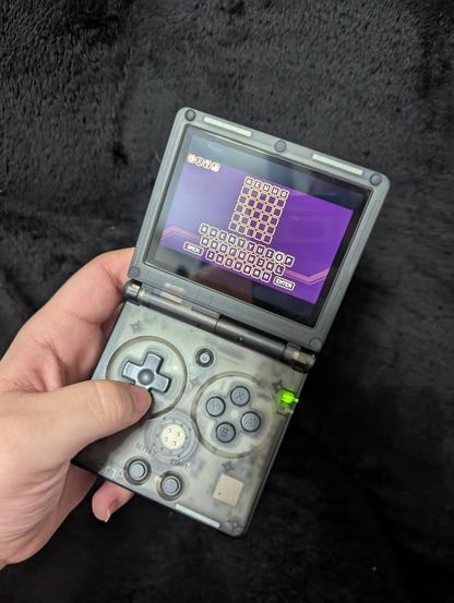 a picture of an anbernic rg35xxsp handheld with words with freds shown on the screen. the inputted word says "hewwo"