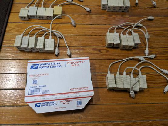 A photo of a USPS flat rate shipping box (white cardboard with blue and red print) next to five groups of five PhoneNET connectors. They are shot from an angle that makes the phone jacks on them clearly visible.