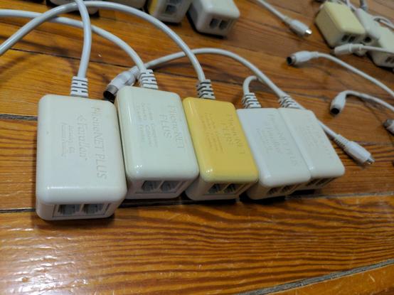 A closeup of five PhoneNET Plus connectors with a few more in the unfocused background. The phone jacks are visible in the foreground and one transceiver is heavily yellowed. Each one has PhoneNET PLUS Farallon Berkeley, CA Patent pending molded into the plastic.