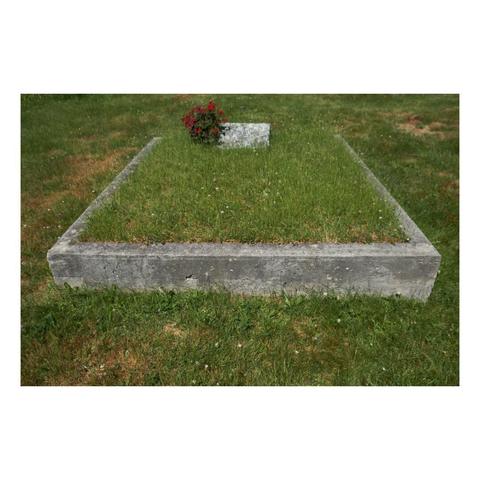 perspective view of square concrete frame sitting above a lawn that contains grass, gravestone, and flowering shrub