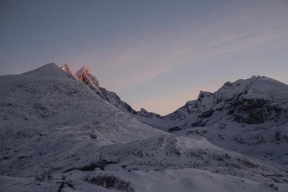 Two mountains full of snow forming a U shape, a little sun hits the top of the left mountain.