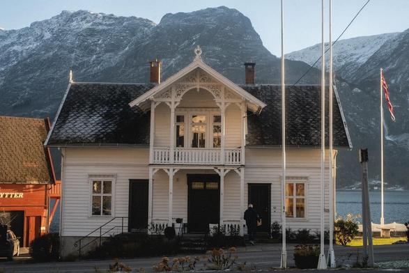 A typical Norwegian house, white with a black rooftop. The fjords behind it.
