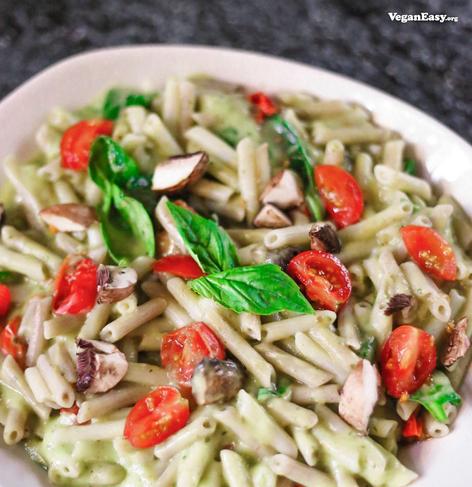 Photo of vegan Creamy Avocado Pasta with mushrooms, spinach and cherry tomatoes.
