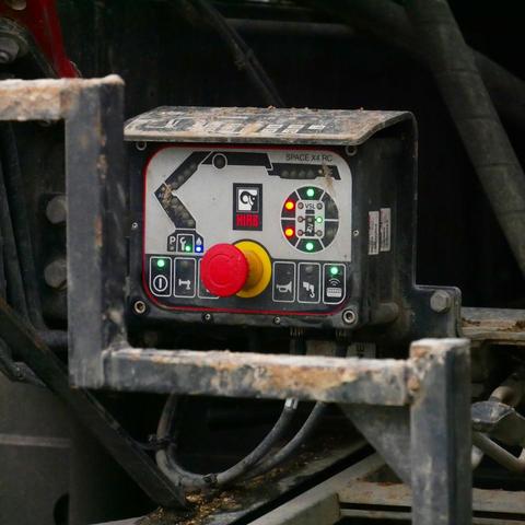 This image shows a control panel for a piece of heavy machinery, specifically a HIAB crane. It features various buttons and indicators, including a large red emergency stop button and a rotary dial with green and red lights. The panel is labeled "SPACE X4 RC."