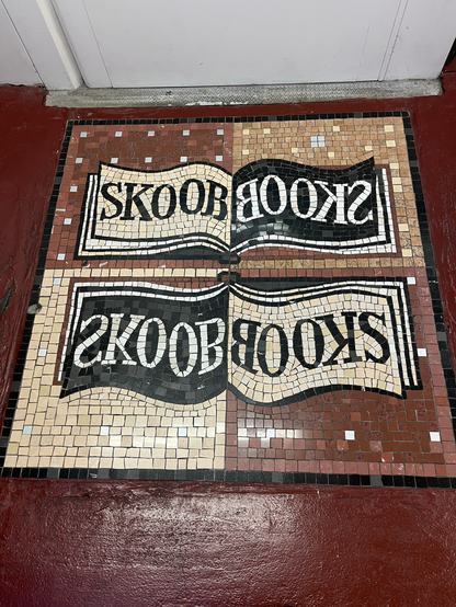 A mosaic of black and white tiles on a rust brown background, spelling out the word SKOOB, which is books, backward. We found it at the entry of a wonderful used bookstore in London’s Bloomsbury neighbourhood. A