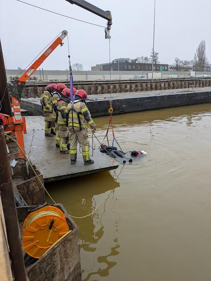 Firefighters assisting the rescue of a diver from a construction site basin with a heavy rescue vehicle crane.