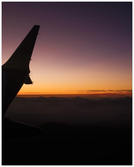 A photo from an airplane showing a part of the wing and the sunrise