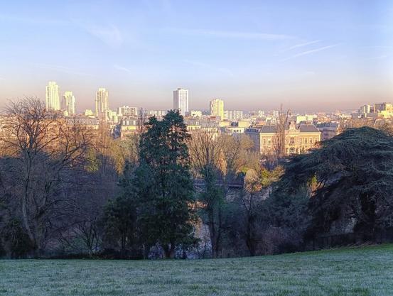 Photo d'un parc, une pelouse au premier plan, avec la ville qui s'étend plus loin à l'horizon. L'herbe est blanchie par le gel mais le ciel est bleu.