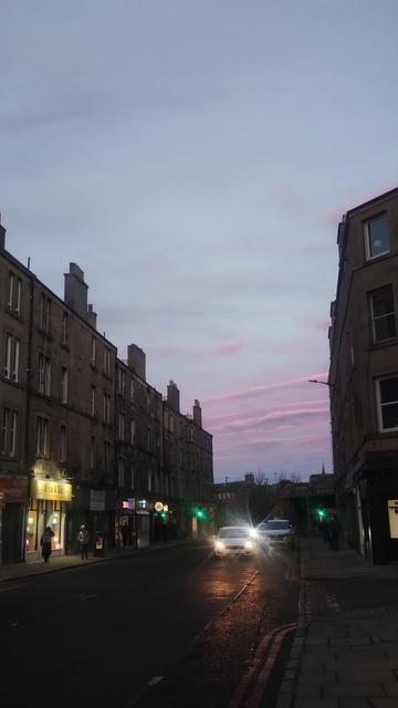 Dusk sky viewed between lines of four storey Victorian stone tenements, pale blue with wispy, pink clouds closer to the horizon
