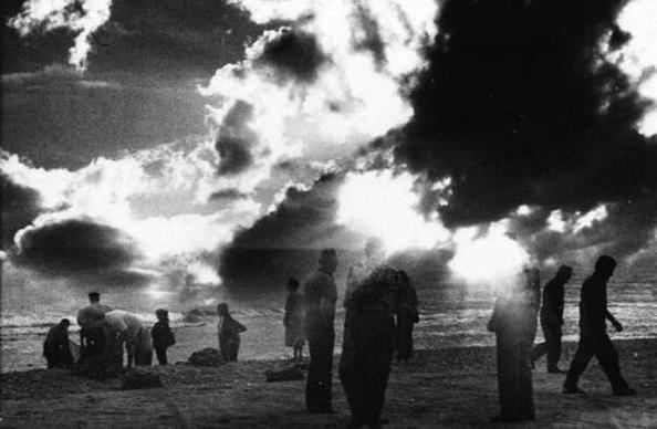 silhouettes of people on beach with sun gleaming through clouds