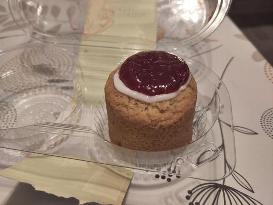 A Runeberg torte in plastic packaging. It's a round, light brown pastry with raspberry jam on top, circled by a white sugar paste. The other torte in the packaging has already been eaten.