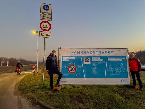 Zwei Mitglieder des AK Mobilität stehen vor dem Info-Banner am Beginn der neuen Fahrradstraße in Umkirch.