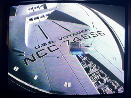 A photo of a CRT TV showing the first episode of Star Trek: Voyager, ‘Caretaker’, playing from a VHS cassette of the episode. Here, small shuttlecraft is flying above USS Voyager.