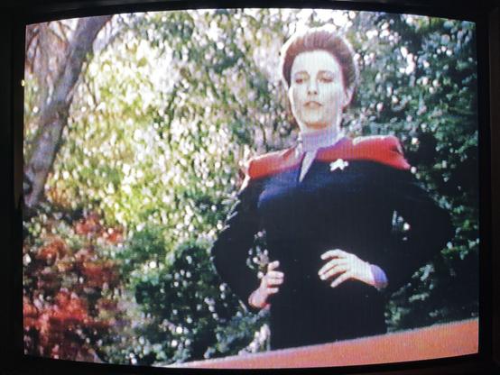 A photo of the episode ‘Caretaker’ of Star Trek: Voyager playing on a VHS cassette and displayed on a CRT TV. This photo shows Capt. Janeway standing hands on hips with woodland behind her and looking down at Tom Paris who is off-screen.