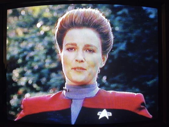 A photo of the episode ‘Caretaker’ of Star Trek: Voyager playing on a VHS cassette and displayed on a CRT TV. This image shows Capt. Janeway standing in front of some woodland and talking to Tom Paris, who is out of shot.