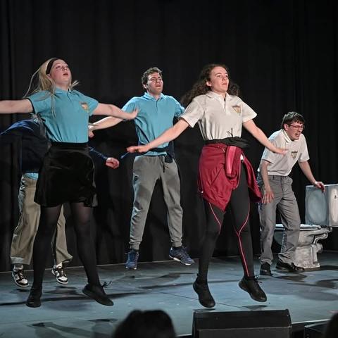 Five young actors defying gravity on a black stage with a toilet....