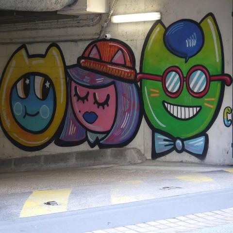 The image shows colorful street art featuring three whimsical cartoon characters on a wall. The characters have unique, stylized features, and each has a distinct, bold color scheme. The artwork includes detailed elements like hats and glasses, giving each character a playful and lively expression.